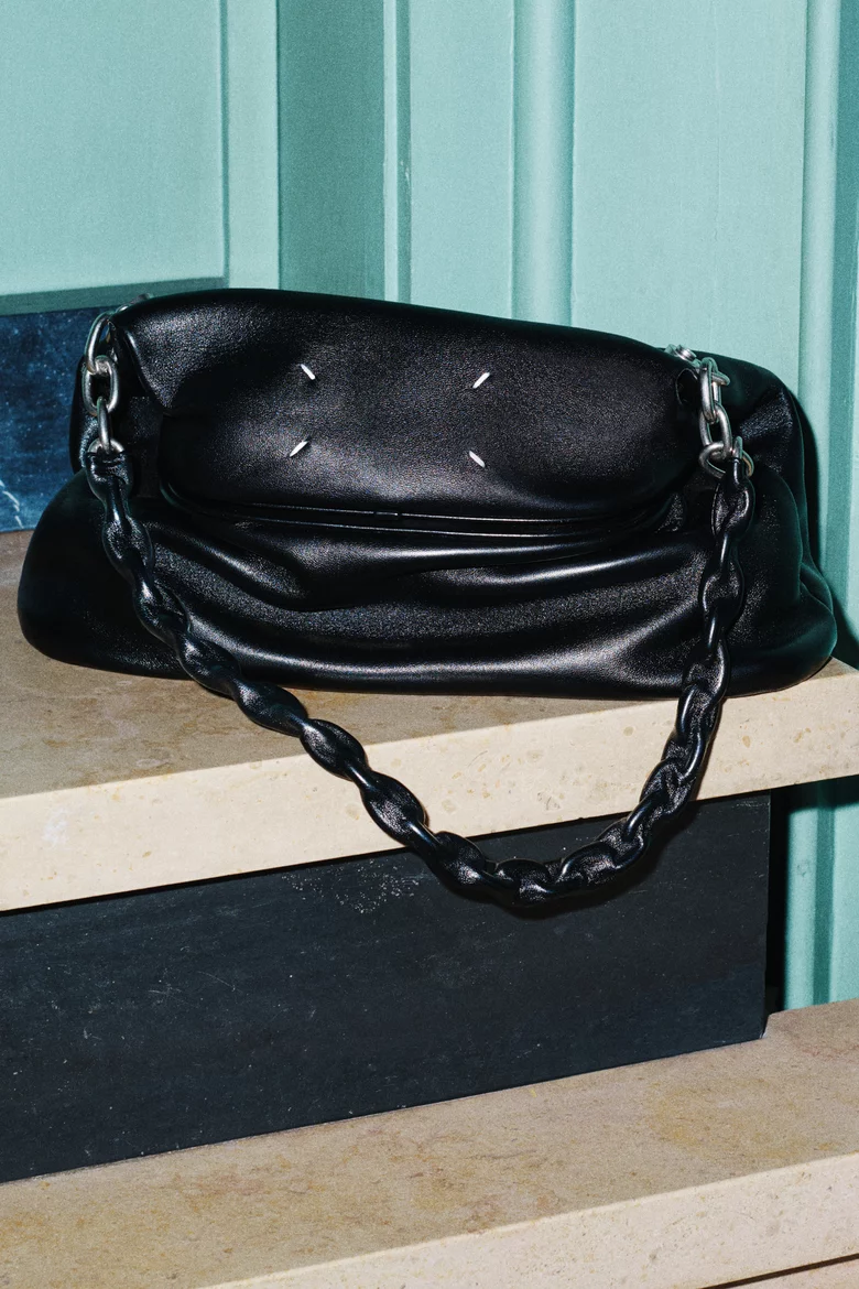 Model carrying a leather shoulder bag with a chain strap